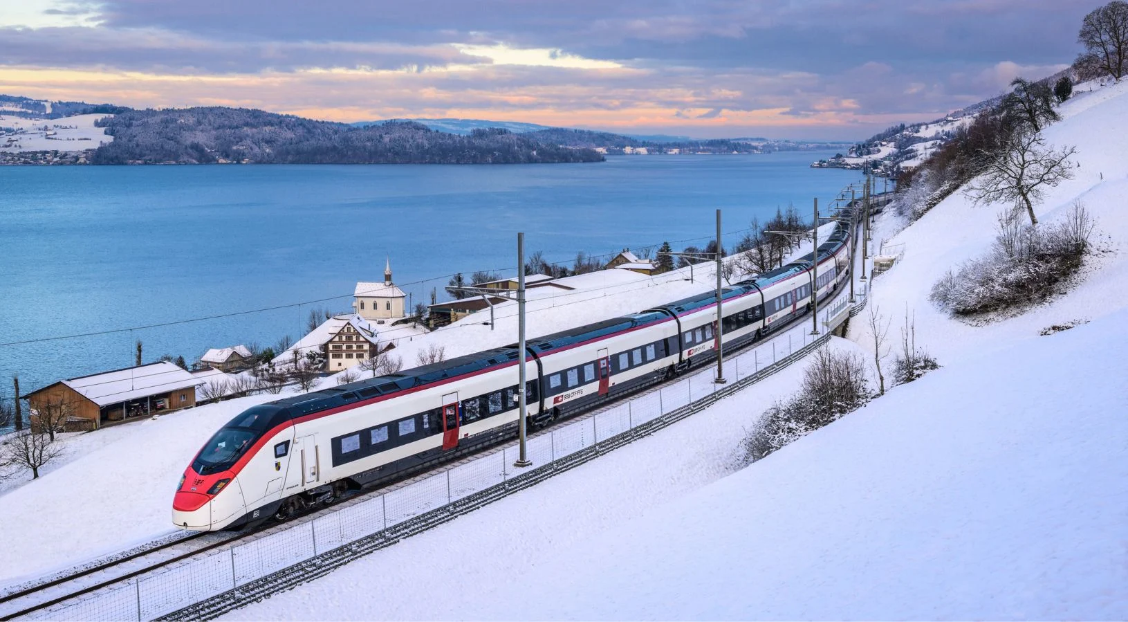 A Swiss panoramic train beside an alpine lake, illustrating the choice between the Swiss Travel Pass and the Swiss Half Fare Card for 2026